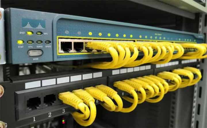 Cisco Catalyst switch in a rack with yellow Ethernet cables and LED status indicators visible